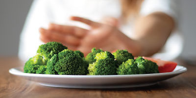 A person rejects a plate of broccoli and tomatoes