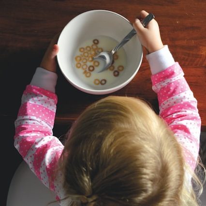 A young child sits at a table with a bowl of milk and cereal.