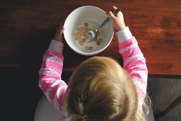 A young child sits at a table with a bowl of milk and cereal.