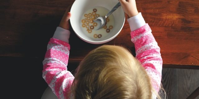 A young child sits at a table with a bowl of milk and cereal.