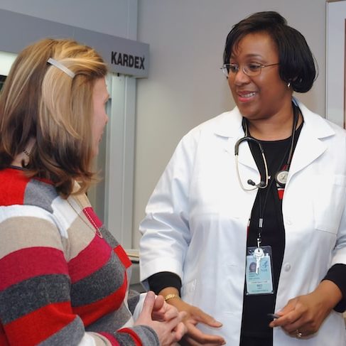 A doctor speaks to a patient sitting in an examination room.