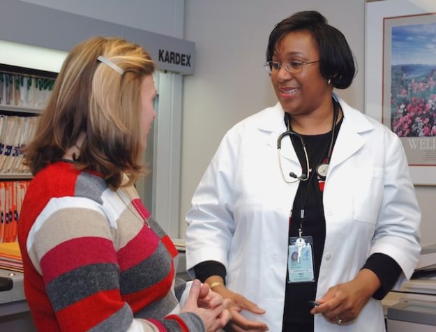 A doctor speaks to a patient sitting in an examination room.