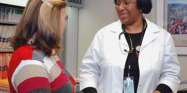 A doctor speaks to a patient sitting in an examination room.