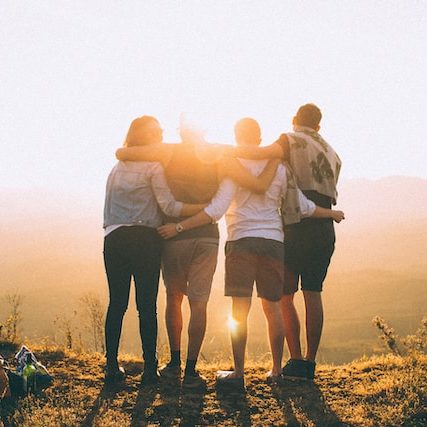 A group of friends stand arm in arm watching the sun set.
