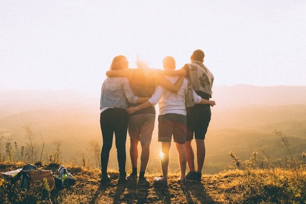 A group of friends stand arm in arm watching the sun set.