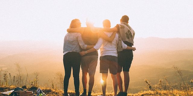 A group of friends stand arm in arm watching the sun set.