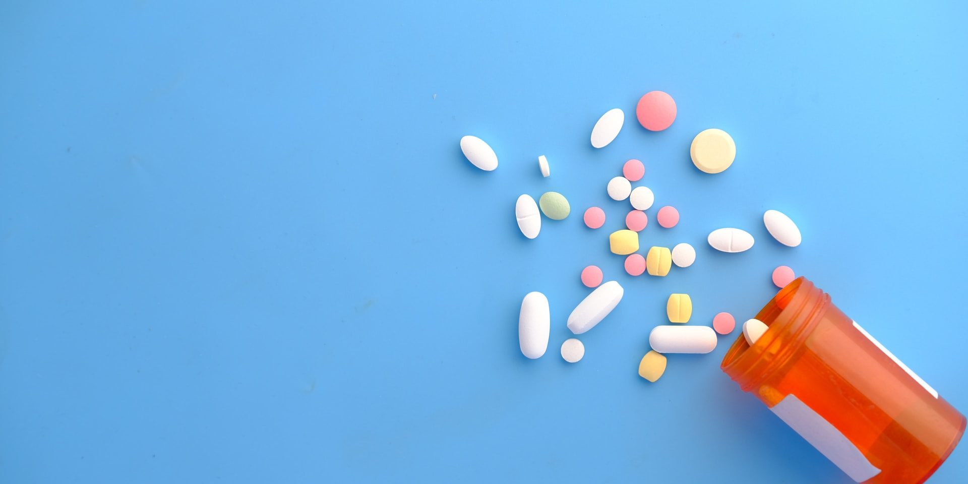 A knocked over prescription bottle, scattering different pills onto a blue surface.