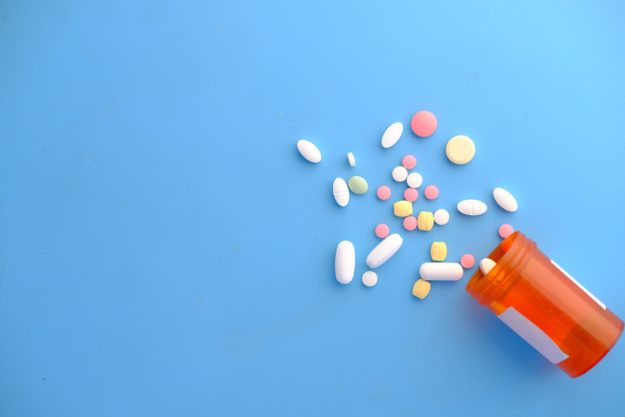 A knocked over prescription bottle, scattering different pills onto a blue surface.
