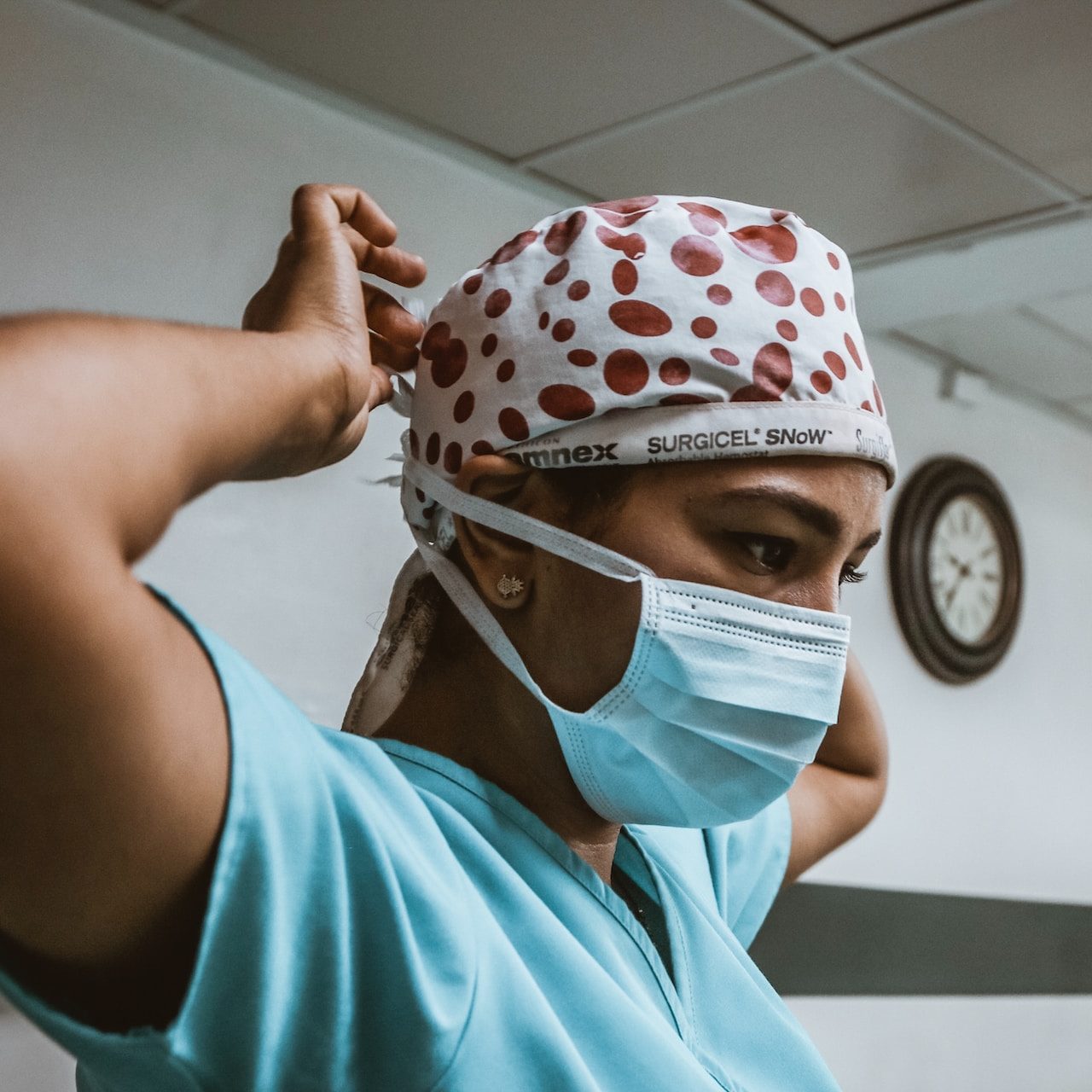 A surgeon wearing medical scrubs secures a face mask around the back of her own head.