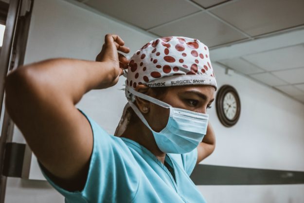 A surgeon wearing medical scrubs secures a face mask around the back of her own head.
