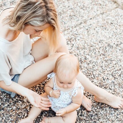 A mother and her baby daughter sit on a beach together.