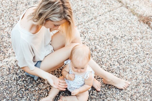 A mother and her baby daughter sit on a beach together.