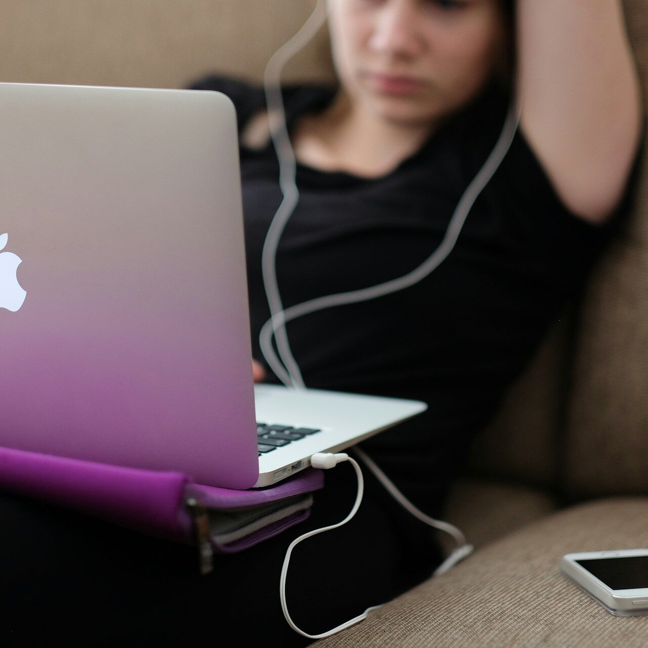 A teenager sitting on a couch, stressed while looking at social media on her laptop.