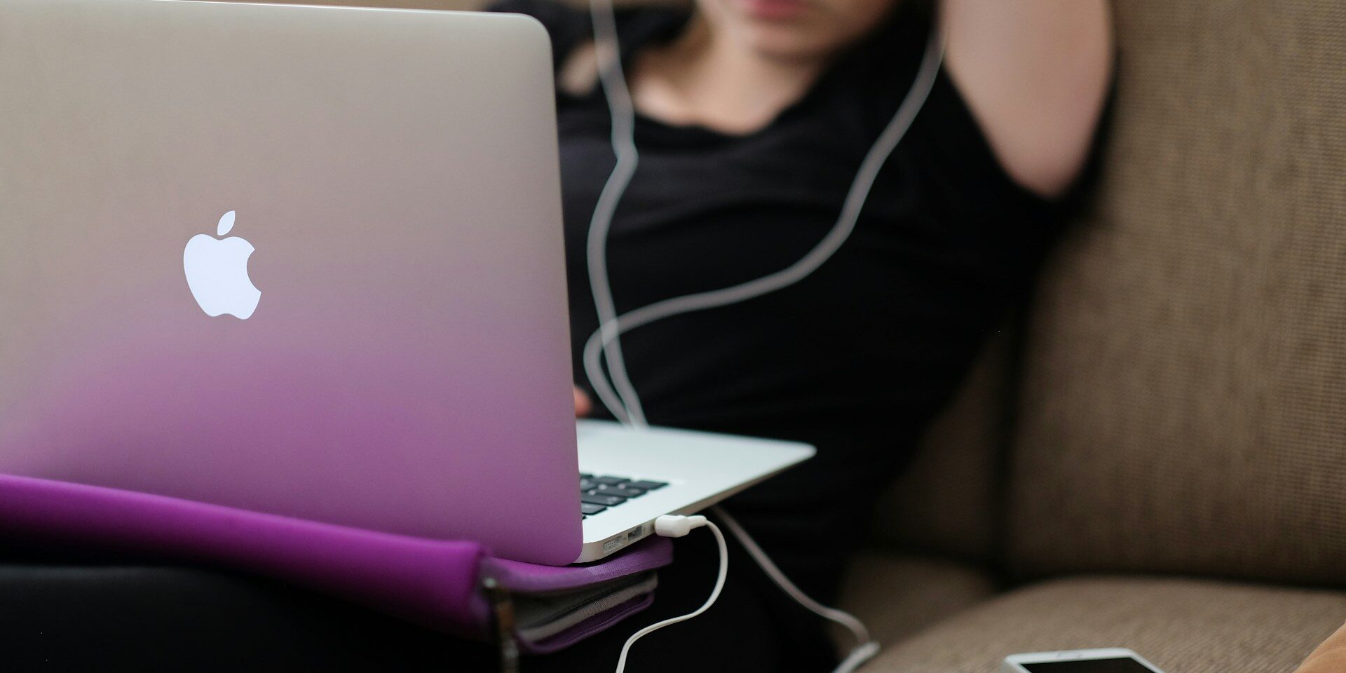A teenager sitting on a couch, stressed while looking at social media on her laptop.