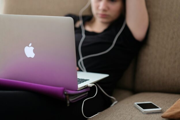A teenager sitting on a couch, stressed while looking at social media on her laptop.