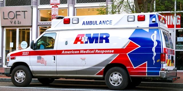 An ambulance parked on the curb outside of various shops.