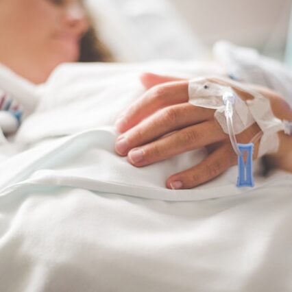 A woman lies in a hospital bed with IV ports taped around her hand.
