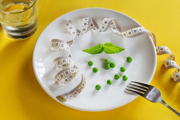 A dining plate with a handful of peas and sprig of mint, along with a tape measure.