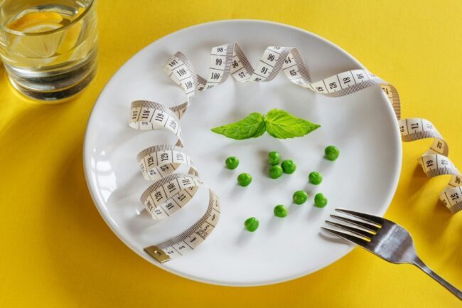A dining plate with a handful of peas and sprig of mint, along with a tape measure.