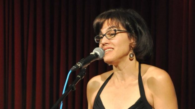 Journalist Abby Ellin on-stage speaking into a microphone.